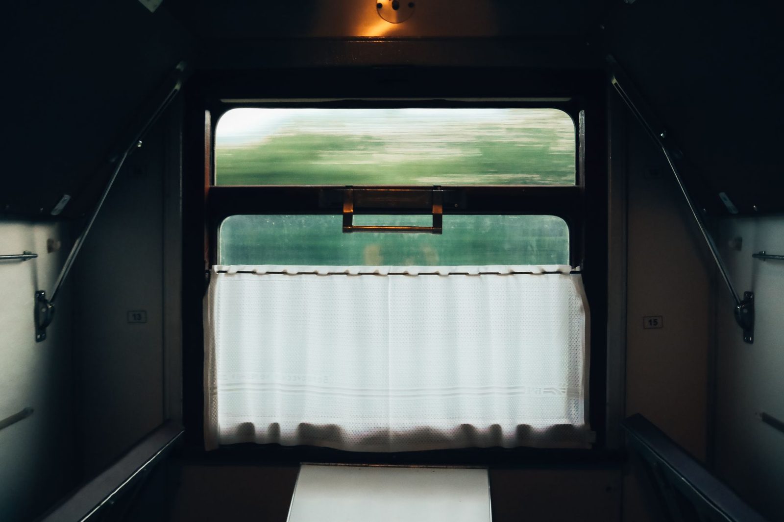 Interior of a train sleeper compartment, window with a white curtain and green landscape rushing past