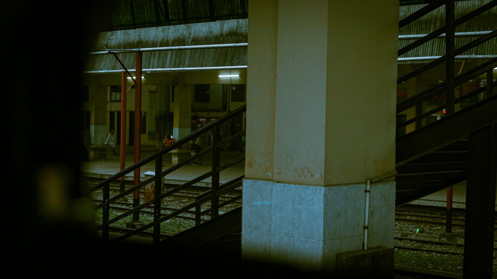 Dimly lit railway platform at night, with a pillar, a metal staircase and train tracks