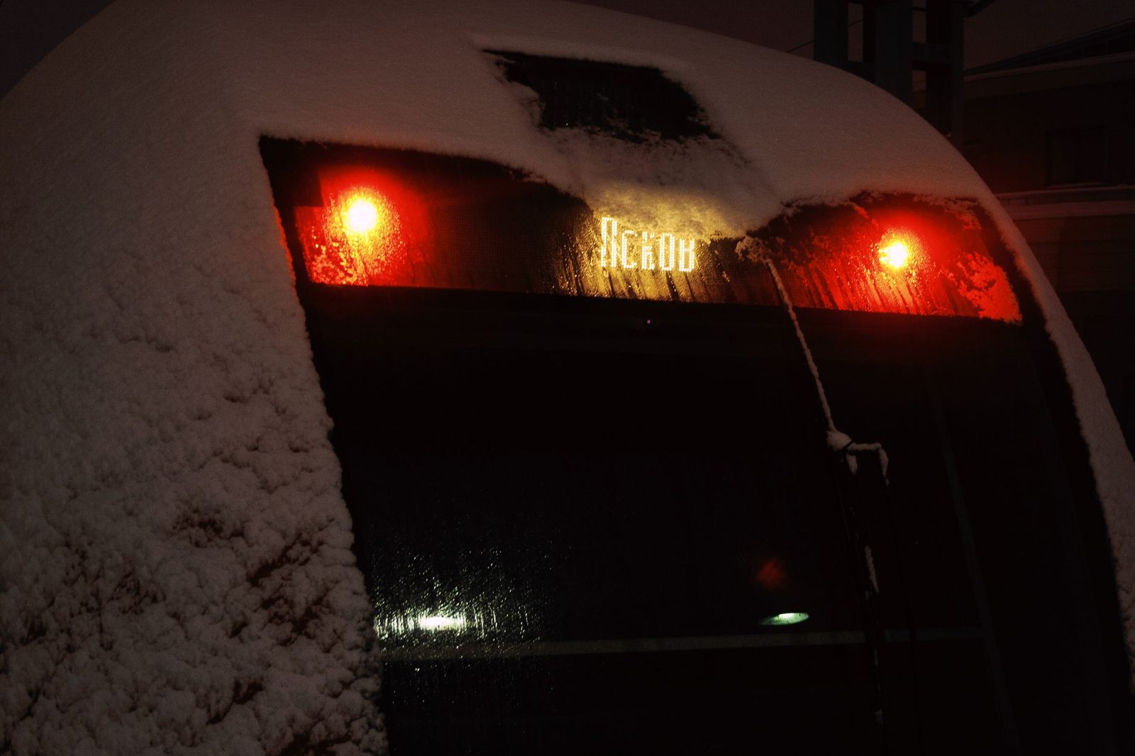 Face avant d'un train couverte de neige la nuit, feux rouges allumés et girouette lumineuse « Pskov »