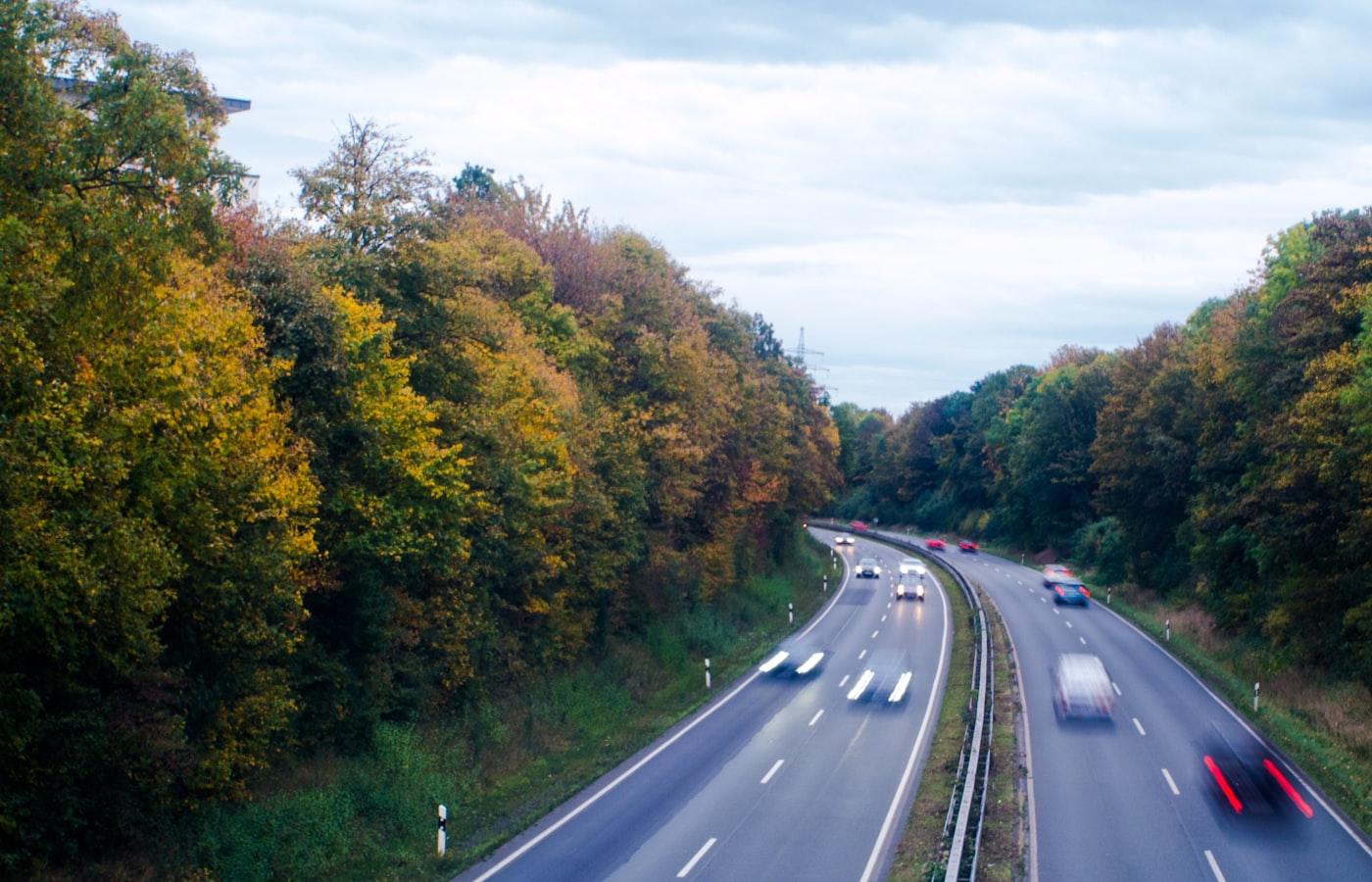 Coches circulando por una autopista europea bordeada de árboles de otoño