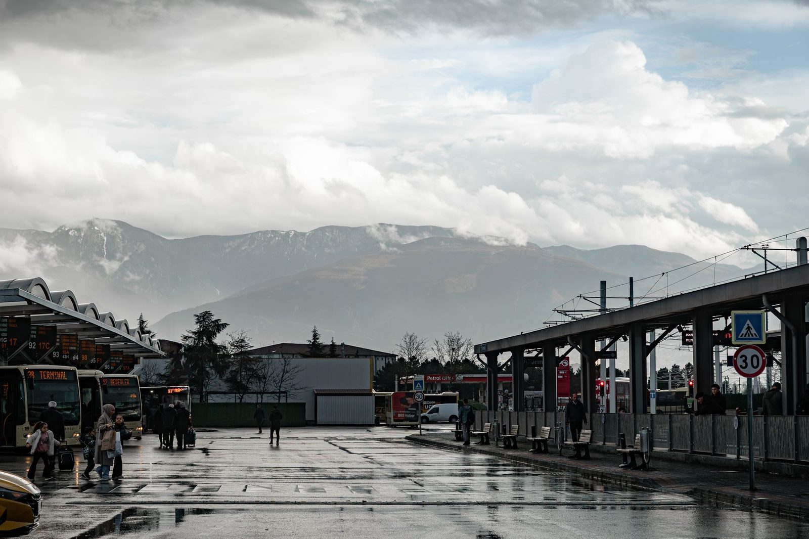 Busbahnhof mit Reisebussen an den Bussteigen und Reisenden, Bahnsteig und nebelverhangene Berge im Hintergrund