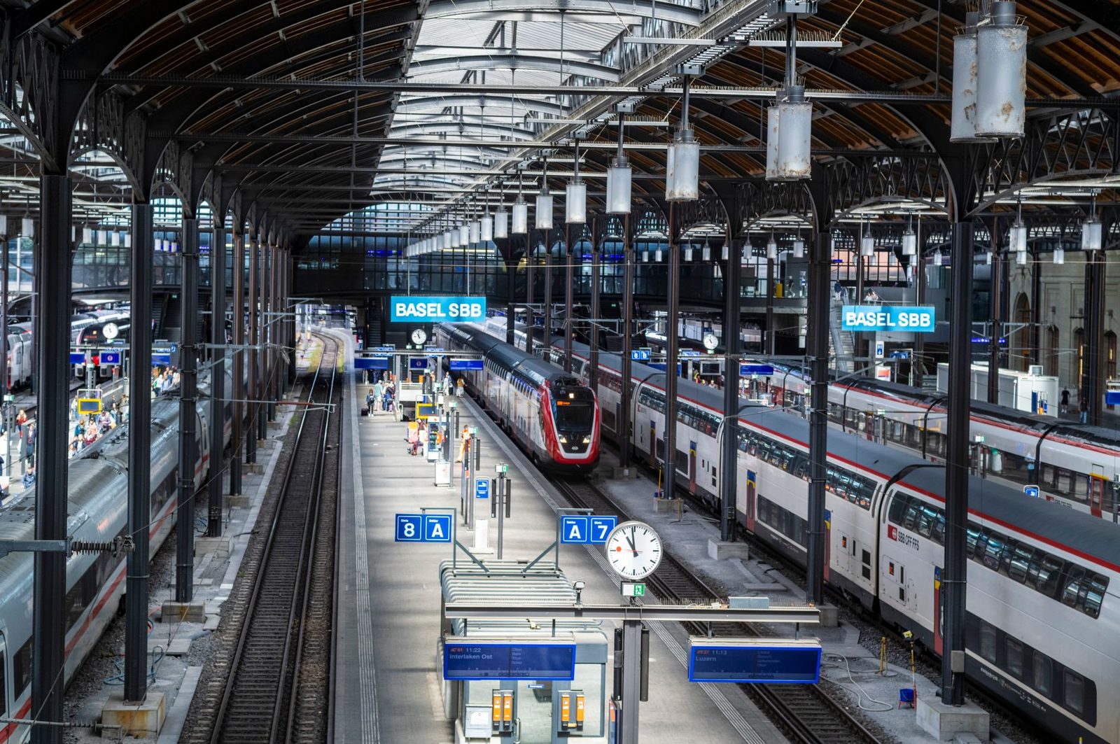 Trains à quai sous la halle de la gare de Bâle CFF, avec panneaux de voies et horloge