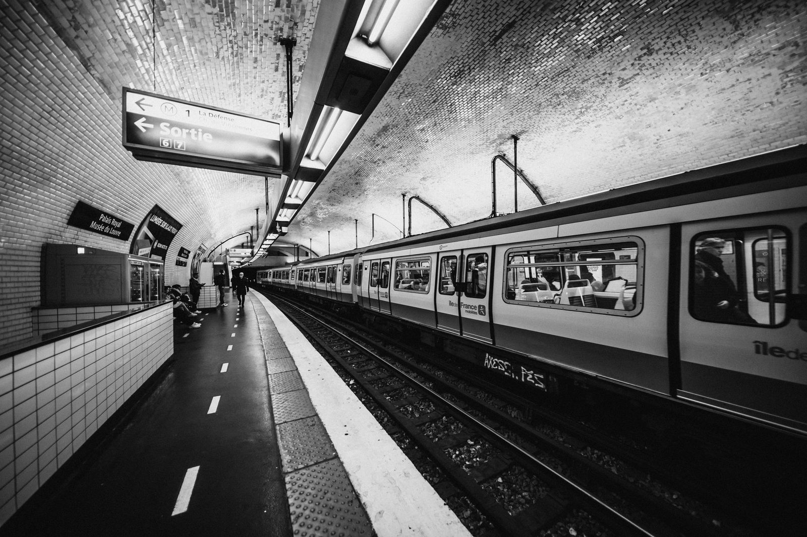 Rame de métro à quai dans une station parisienne carrelée, panneau « Sortie » en noir et blanc