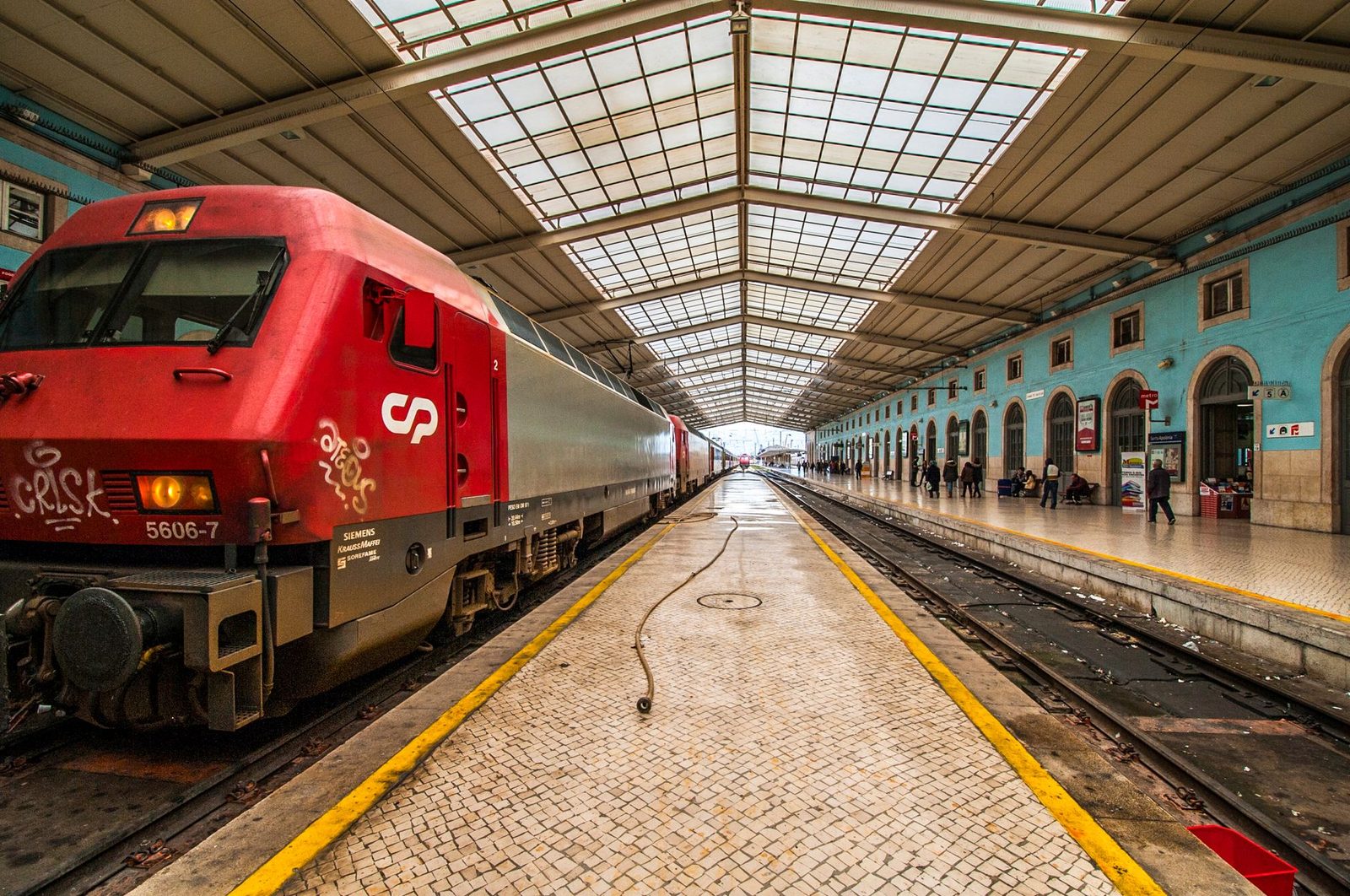 Locomotive rouge CP à quai sous la verrière d'une gare ferroviaire, voyageurs au loin