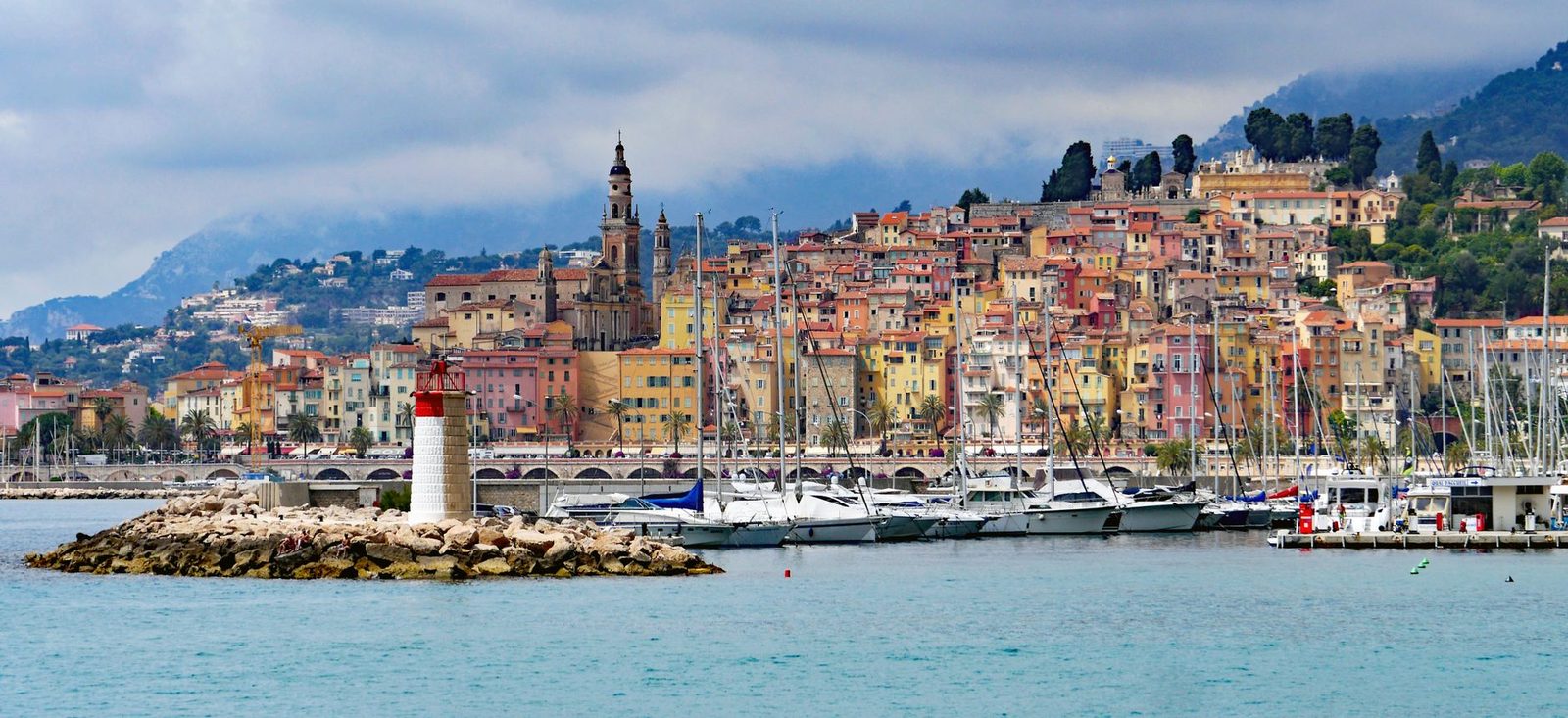 Vista del puerto de Menton con su faro rojo y blanco, sus barcos y el casco antiguo de fachadas de colores