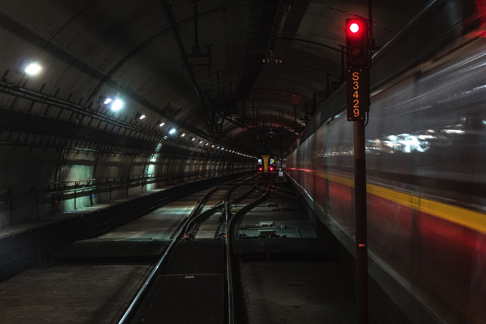 Fahrender Zug in einem beleuchteten Eisenbahntunnel mit rotem Signal S3429 und zusammenlaufenden Gleisen