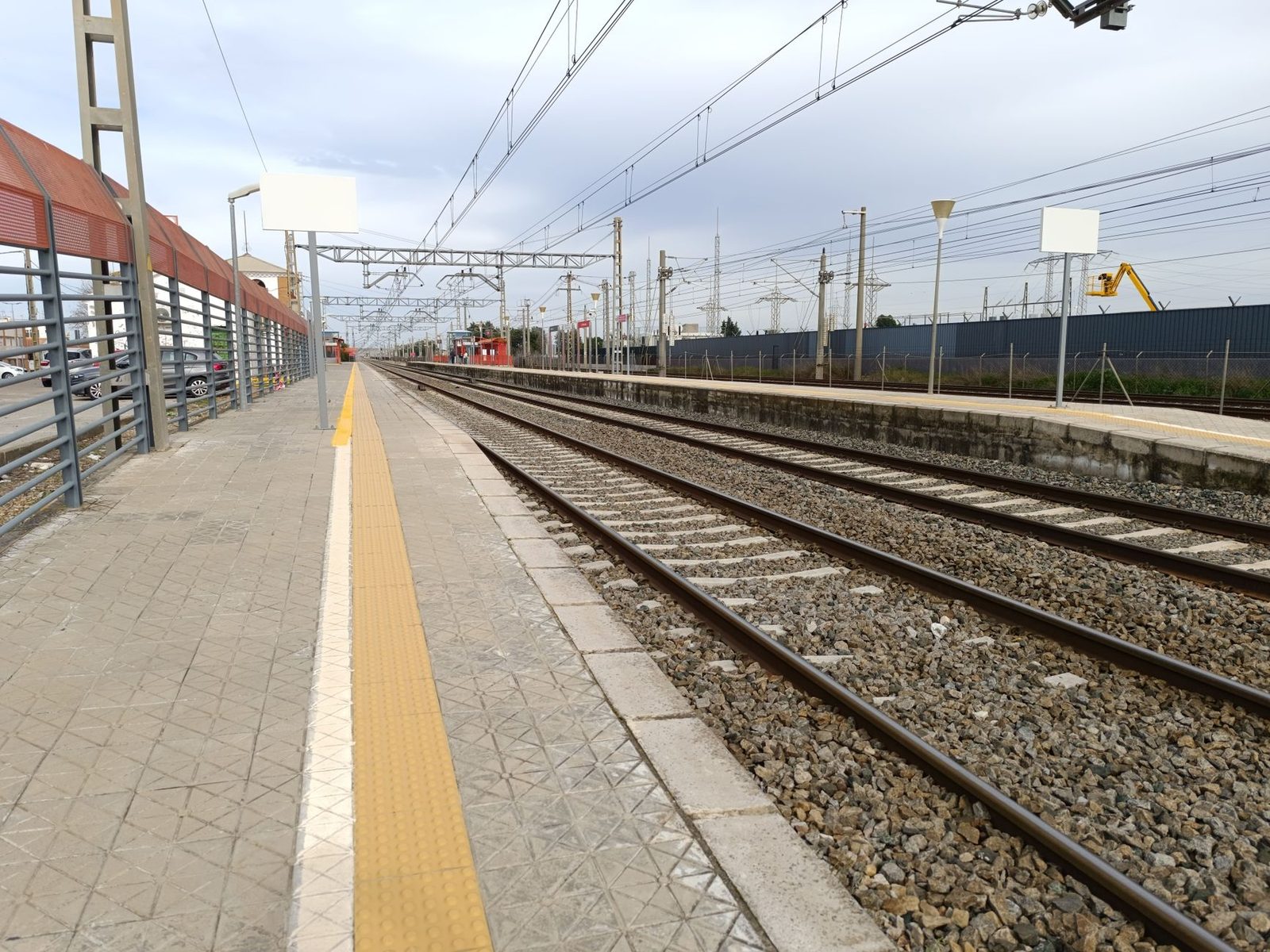 Leerer Bahnsteig mit elektrifizierten Gleisen und Oberleitungen, die sich bis zum Horizont erstrecken