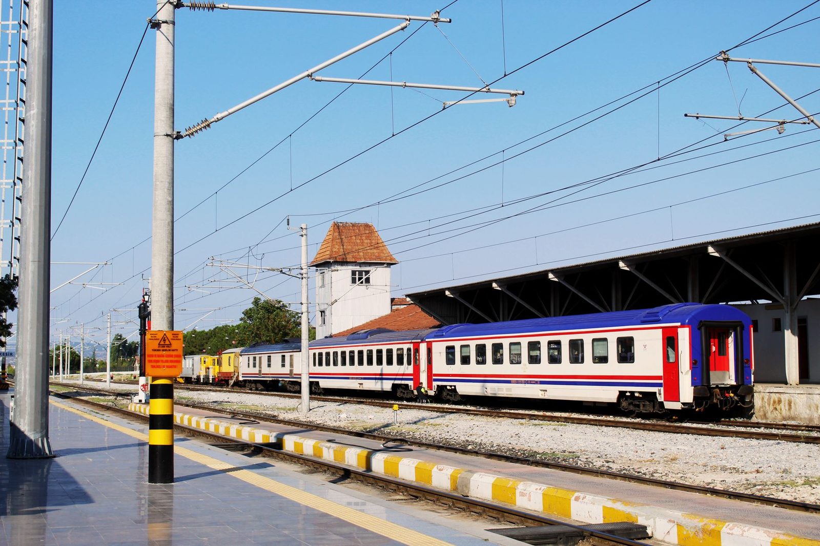 Train de voyageurs bleu, blanc et rouge à quai sous caténaires dans une gare ensoleillée