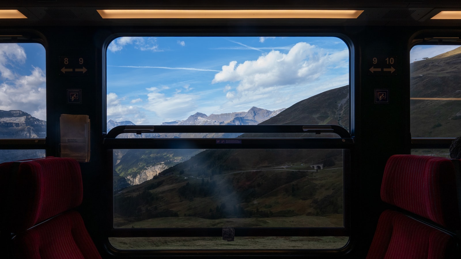 Blick auf die Alpen durch das Fenster eines europäischen Panoramazugs mit roten Sitzen