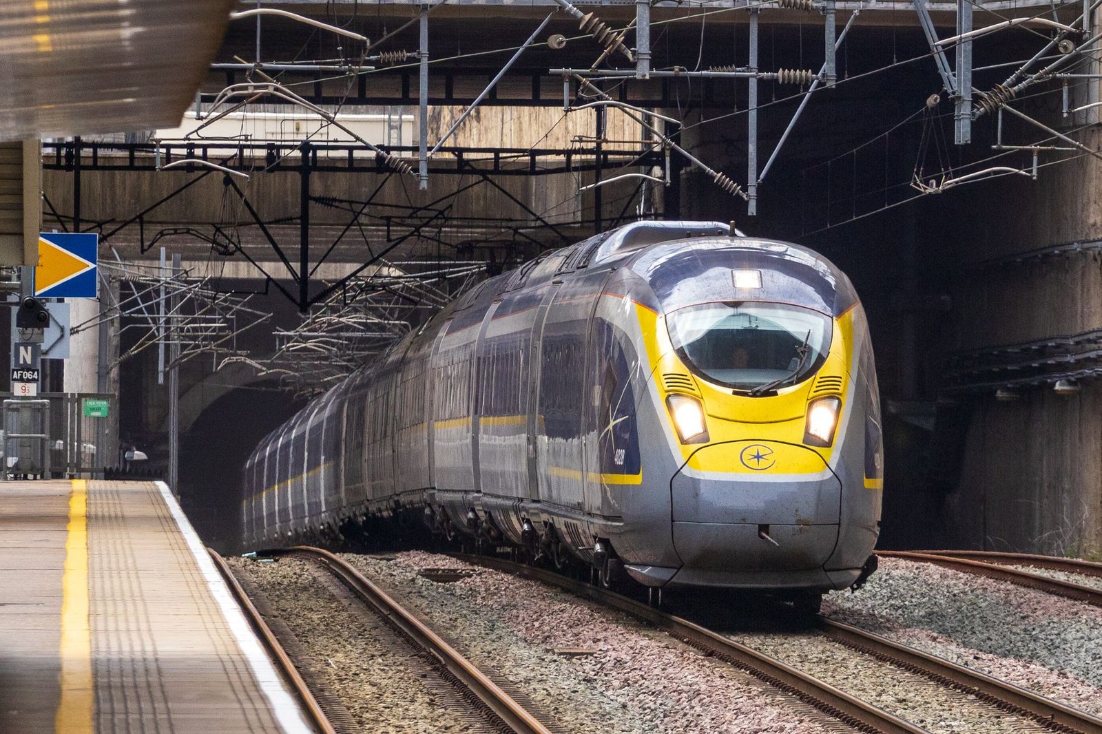 Grau-gelber Eurostar-Hochgeschwindigkeitszug fährt unter Oberleitungen entlang eines Bahnsteigs in den Bahnhof ein