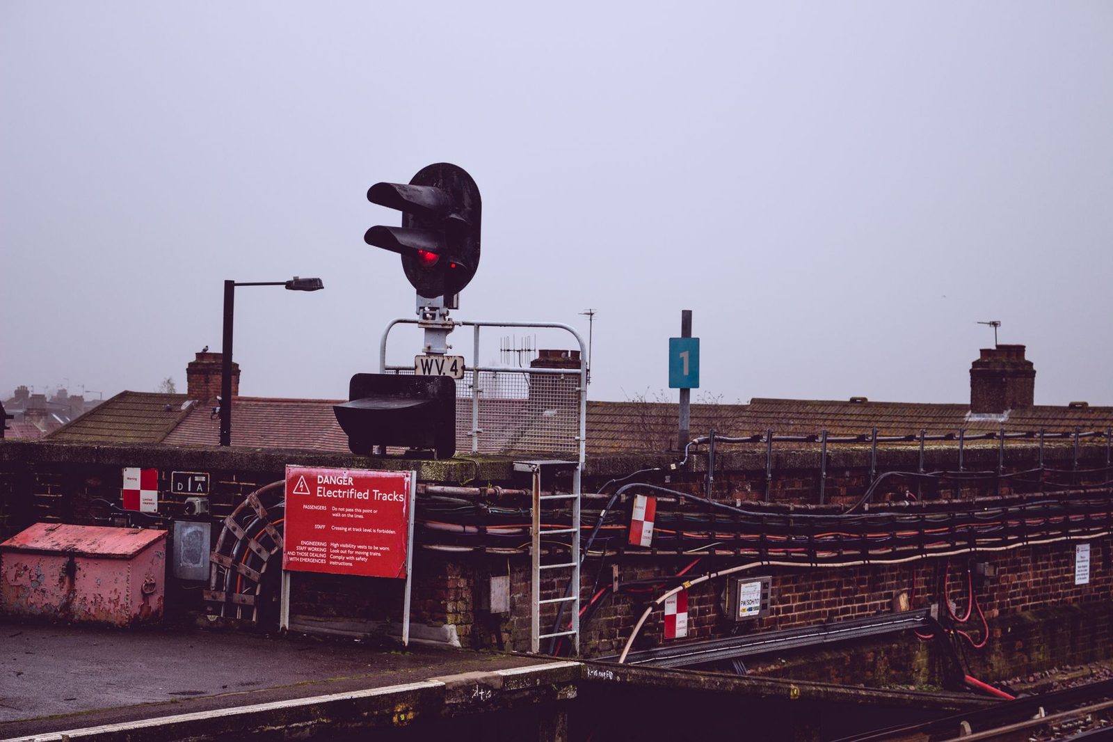 Railway signal at red and a "Danger Electrified Tracks" sign on a misty station platform