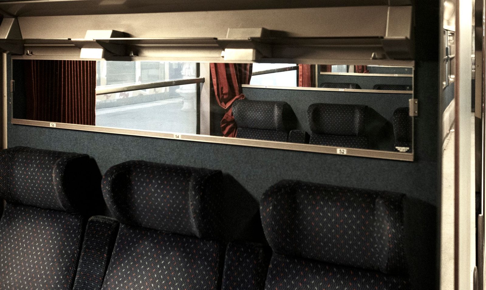 Interior of a train carriage with dark fabric seats and a window looking onto a platform
