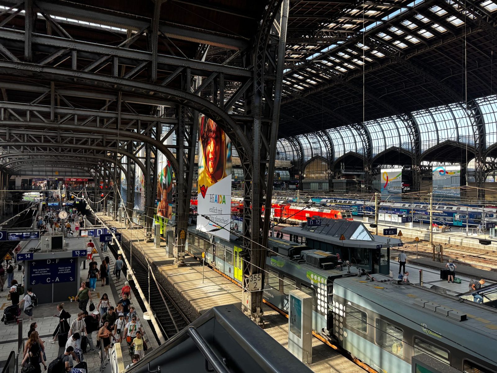 Overhead view of the platforms and trains of a large European railway station beneath a metal-framed glass roof
