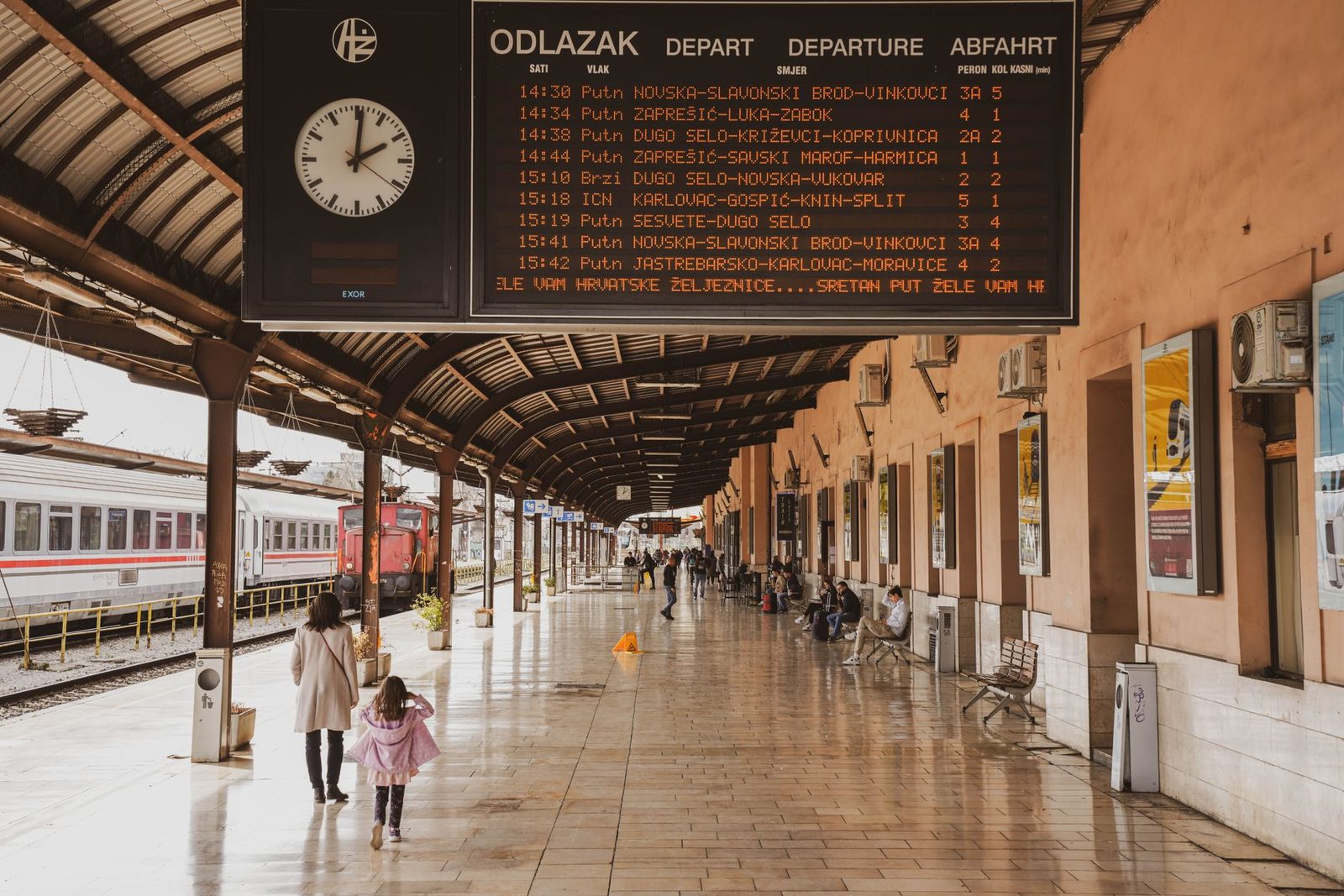 Station platform with a train departure board, travellers and a stationary train