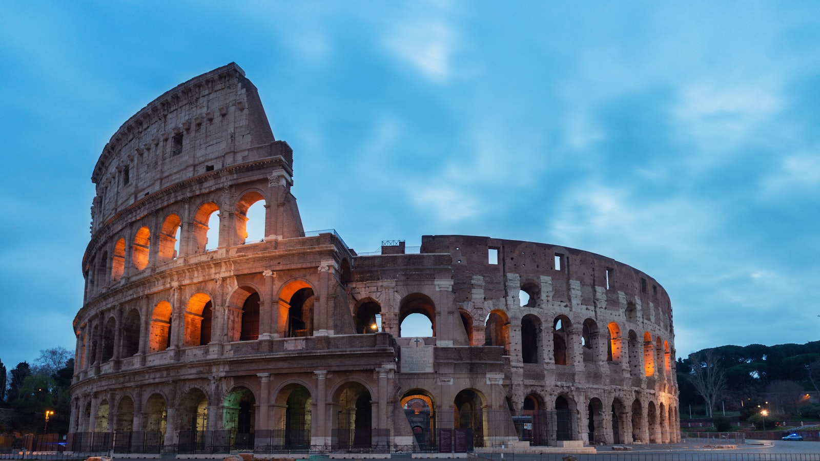 The Colosseum in Rome lit up at dusk under a blue sky