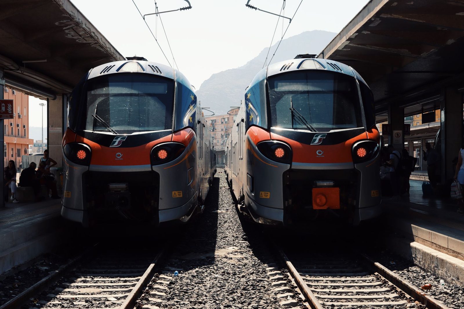 Deux trains régionaux orange et gris face à face en gare, voyageurs sur les quais sous les caténaires
