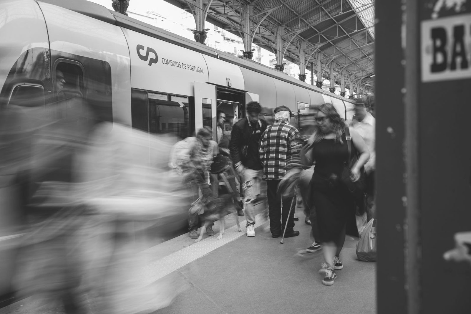 Schwarzweißfoto von Reisenden, die unter dem Glasdach eines Bahnhofs aus einem Zug am Bahnsteig aussteigen