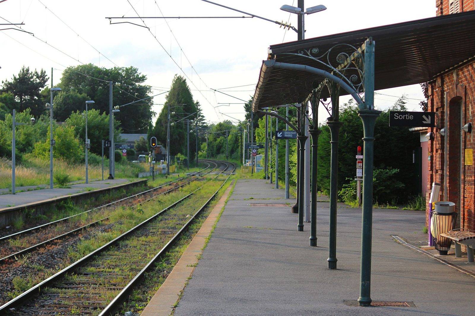Empty platform at a small French station with a canopy, railway tracks and "Sortie" and "Direction Paris" signs