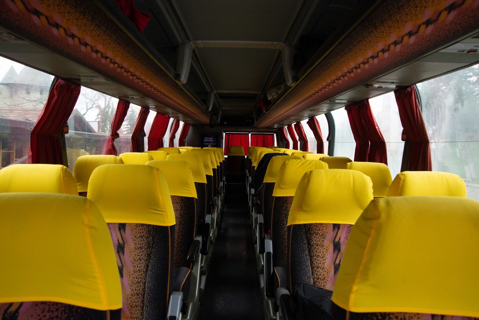 Intérieur d'un autocar avec rangées de sièges jaunes, allée centrale et rideaux rouges aux fenêtres