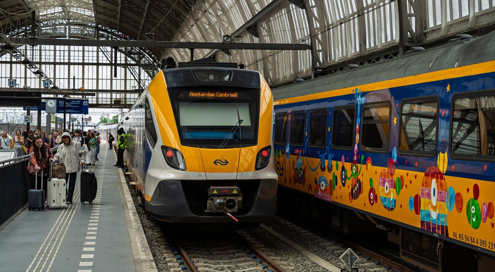 Trains at the platforms of Amsterdam Centraal station, travellers with suitcases walking along the platform