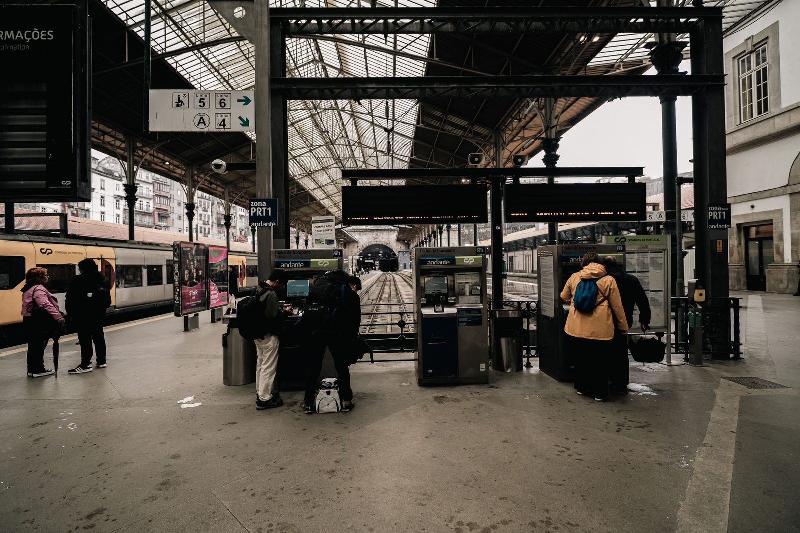 Travellers in front of ticket machines on a railway station platform, with a train standing at the platform