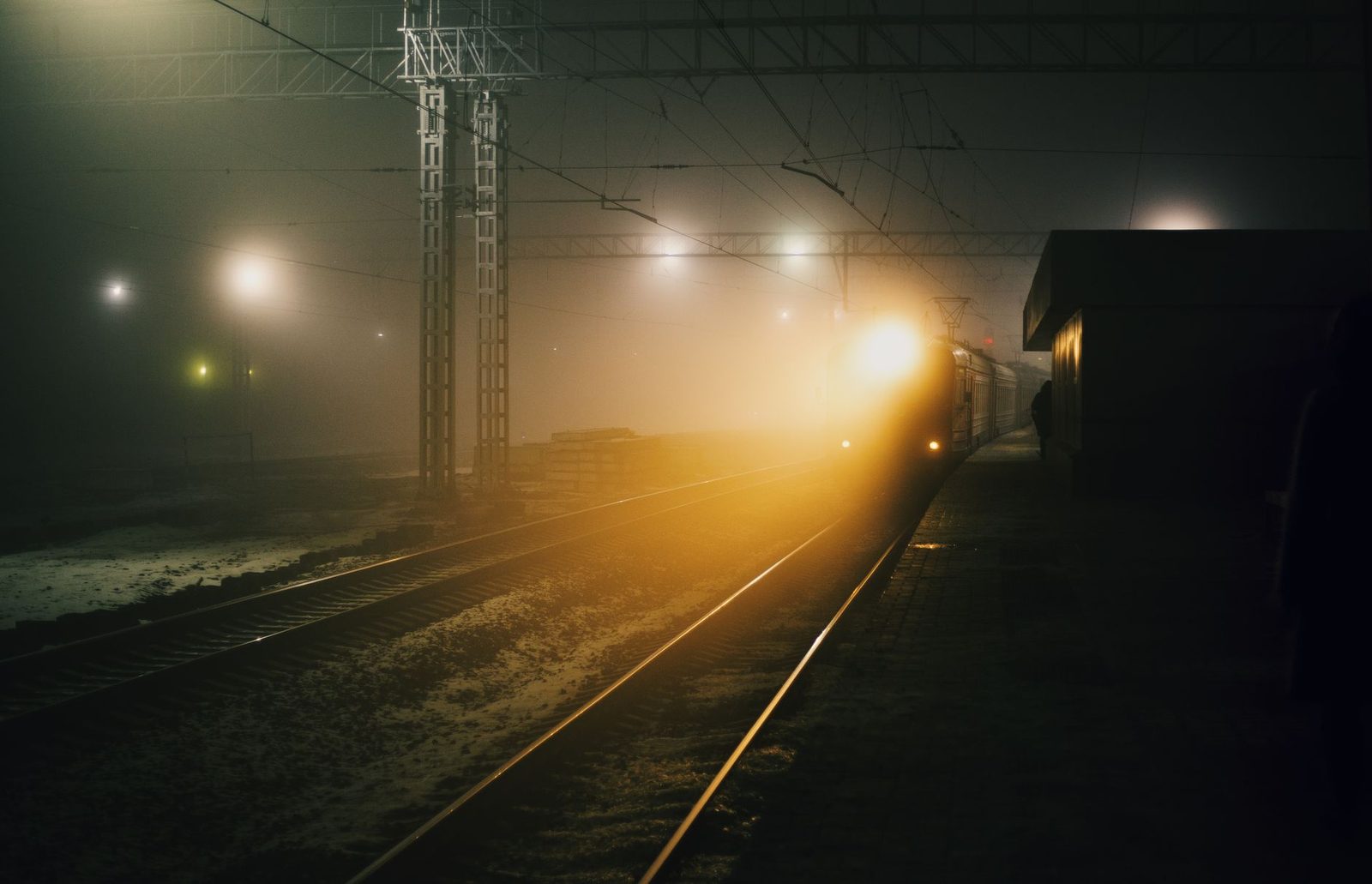 Zug, der nachts im Nebel entlang eines beleuchteten Bahnsteigs einfährt, Scheinwerfer an