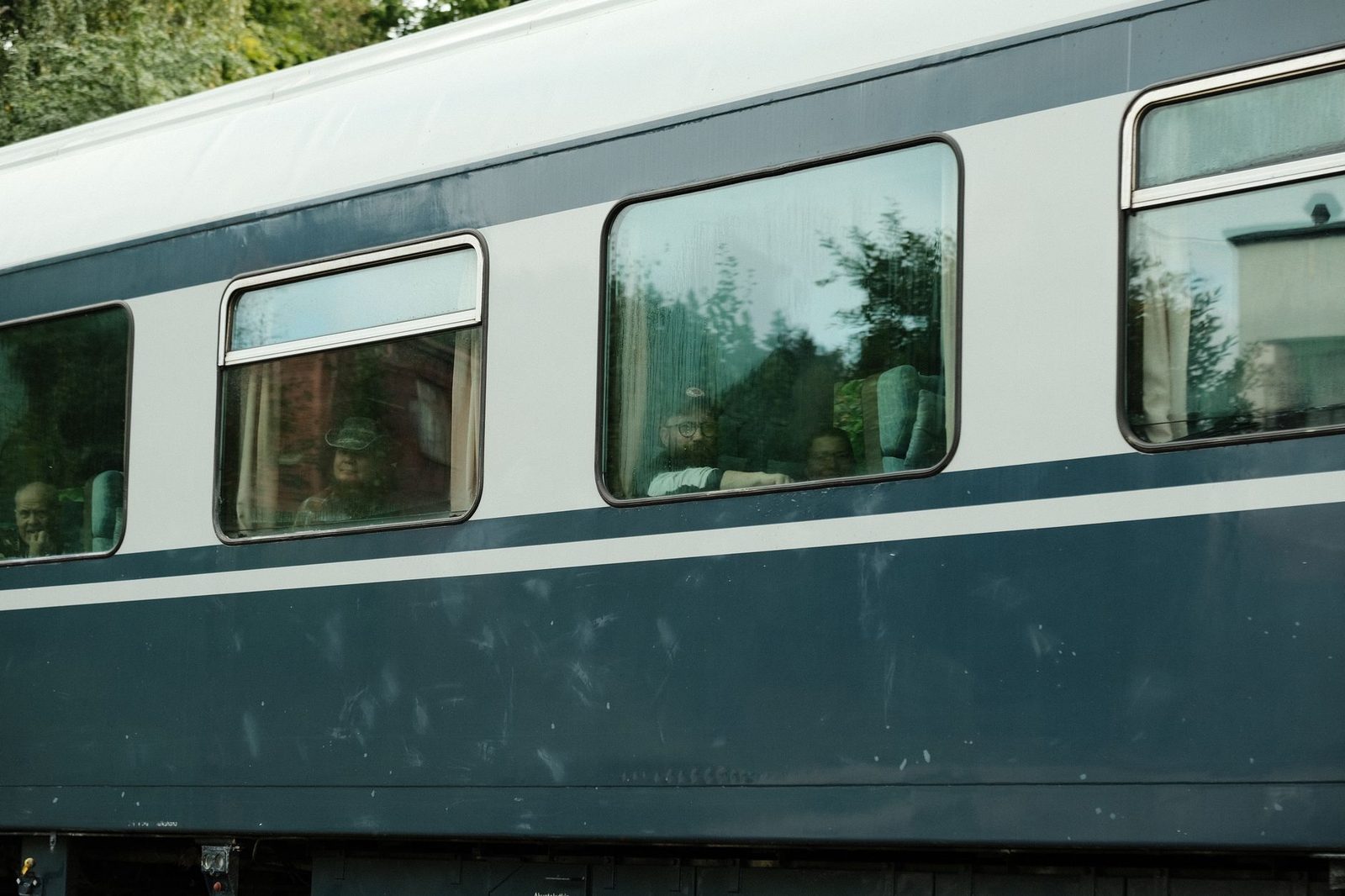 Blau-weißer Eisenbahnwagen mit Fahrgästen hinter den Fenstern