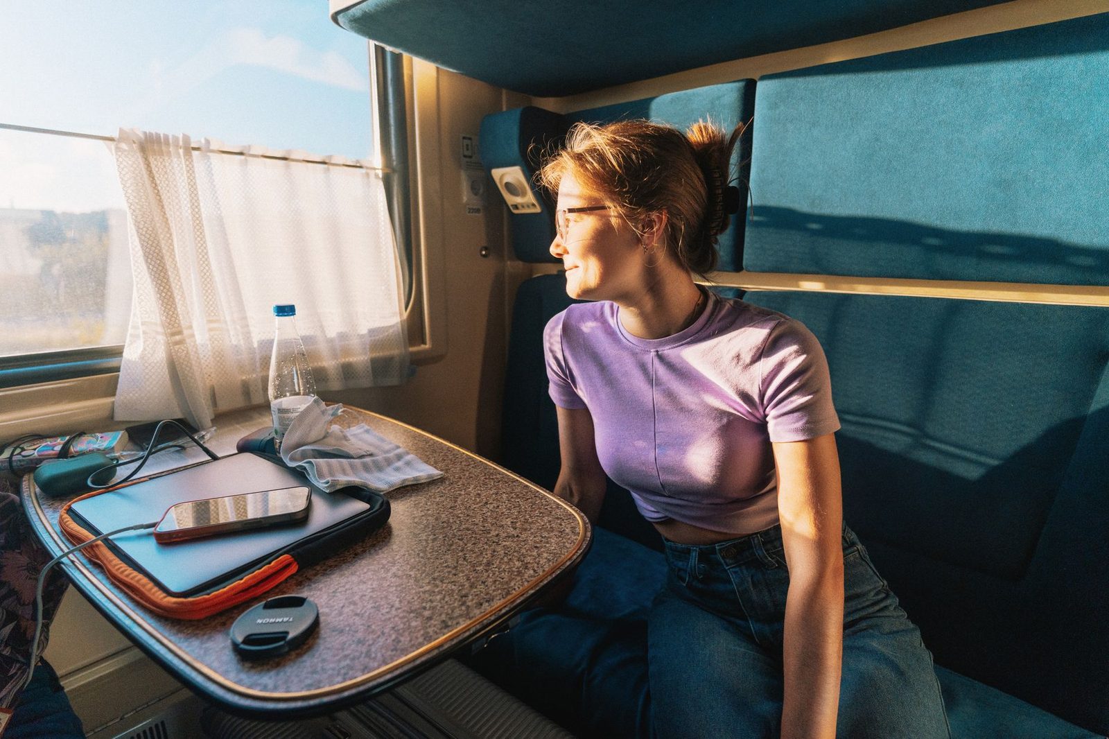 Young woman sitting in a couchette compartment, looking out of the window at sunrise