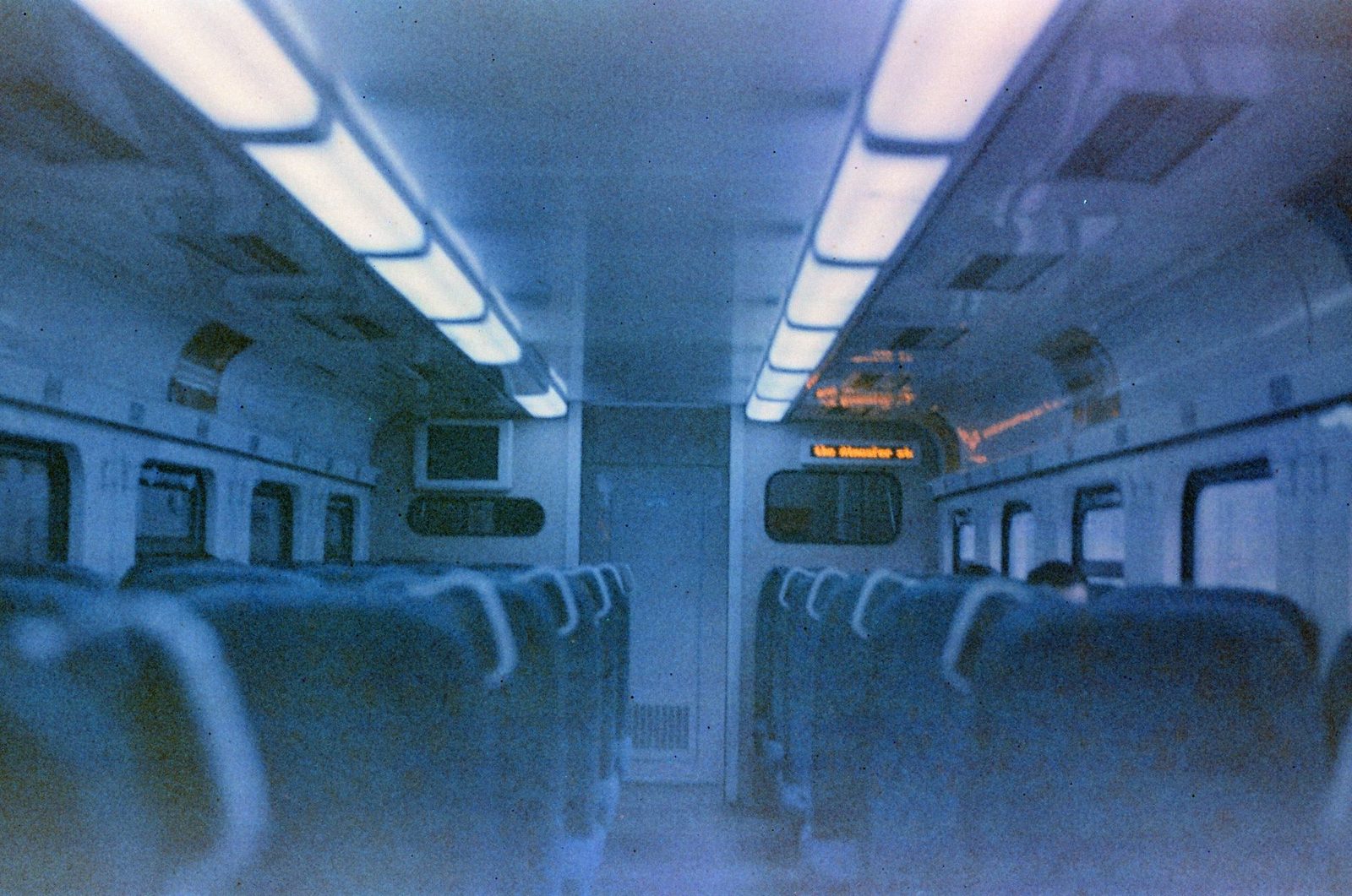 Dark interior of an empty train carriage, rows of seats and blue-tinted ceiling lighting