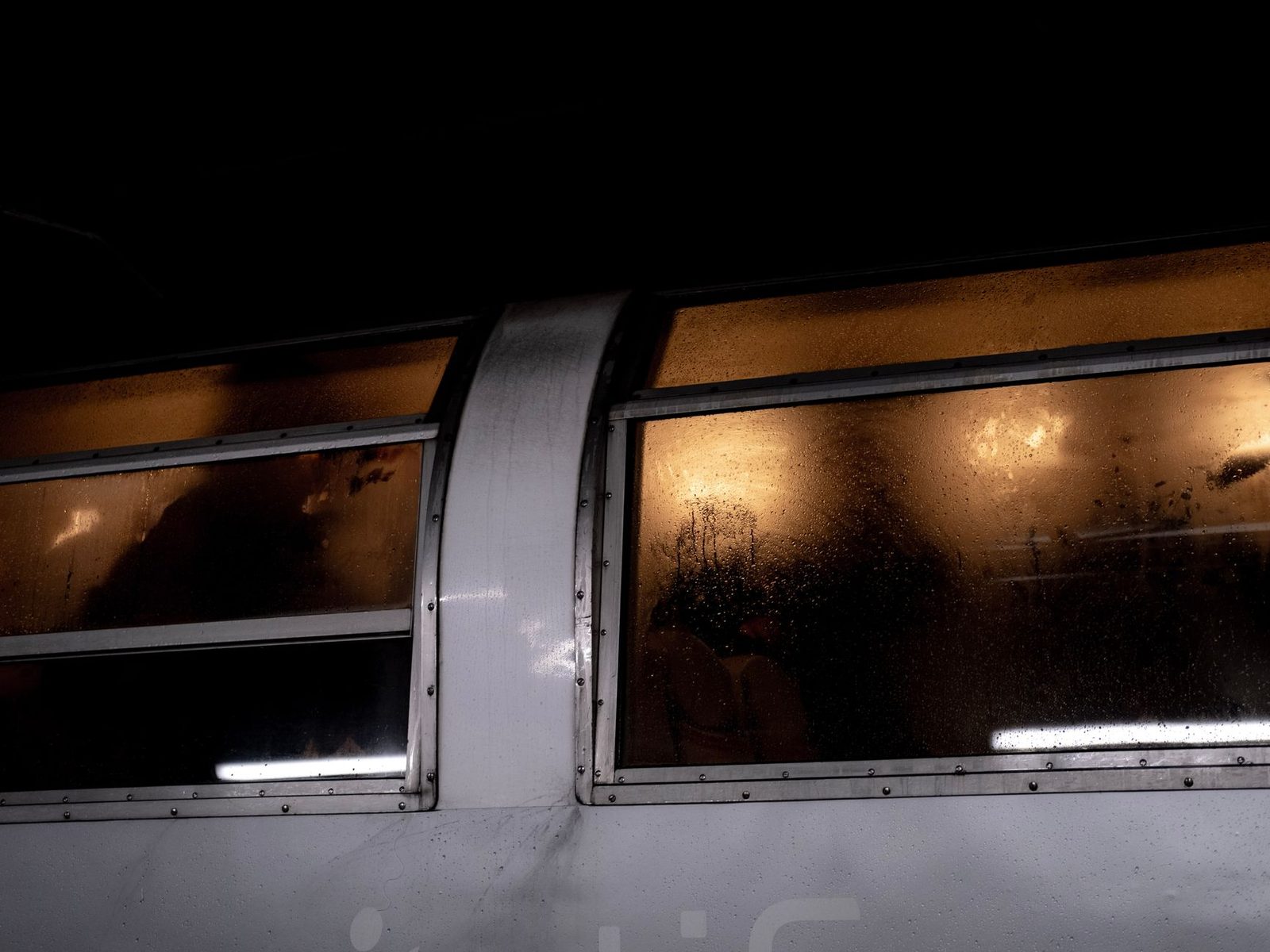 Fogged-up windows of a lit train carriage at night, silhouettes of passengers inside