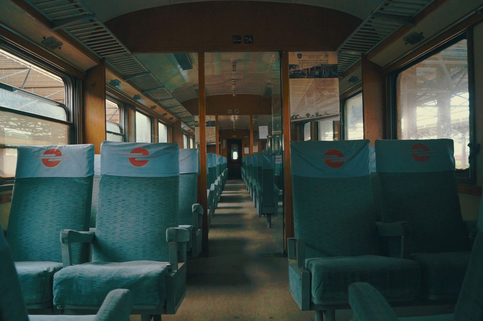 Interior of an empty train carriage with green seats and white headrests, wooden central aisle